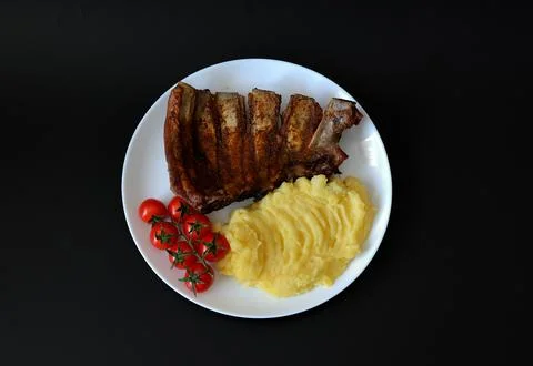 Baked pork ribs with mashed potatoes and cherry tomatoes on a round plate a.. Stock Photos