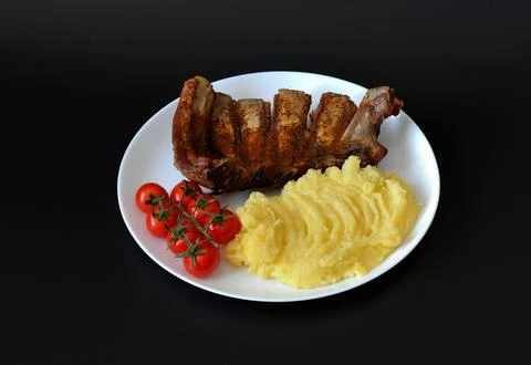 Baked pork ribs with mashed potatoes and cherry tomatoes on a vine in a rou.. Stock Photos