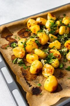 Baked potatoes sit on a baking sheet sprinkled with herbs. This dish serves.. Stock Photos