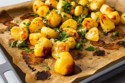 Baked potatoes sit on a baking sheet sprinkled with herbs. This dish serves a Stock Photos