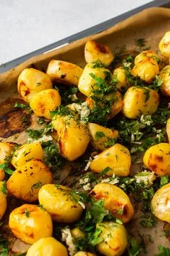 Baked potatoes sit on a baking sheet sprinkled with herbs. This dish serves a Stock Photos