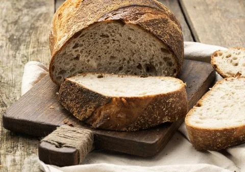 Baked round bread made from white wheat board on wooden board, loaf cut int.. Stock Photos