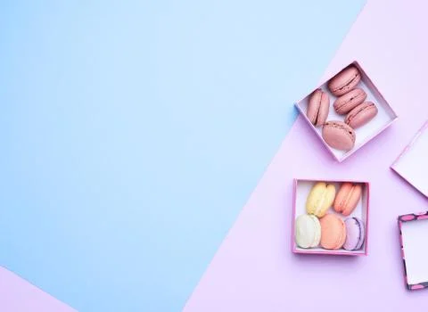 Baked round multicolored macarons in square boxes on a colored pastel backgro Stockfoto's