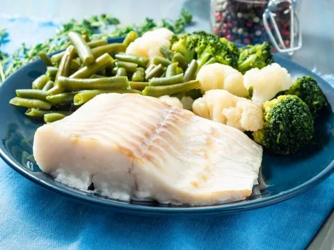Baked sea fish cod fillet with vegetables on blue plate, blue napkin, side .. Stock Photos