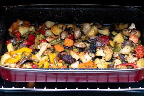 Baked vegetables on a red baking sheet..Vegetable stew on a baking sheet in t Stock Photos