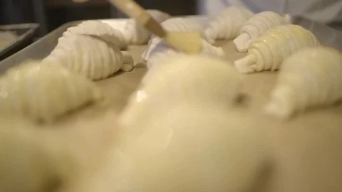 Baker applying egg wash over the rolled croissant dough with a brush Stock Footage 87613012