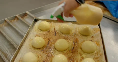 Baker applying glaze to proofed dough on stained baking tray in commercial Stock Footage 344583433