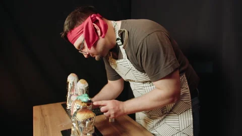 Baker in apron and red headband carefully spoons green icing onto the baked good Stock Footage 330537233