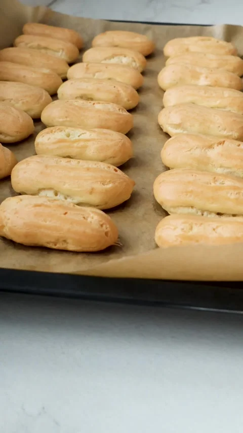 Baker arranging golden choux pastry shells on baking tray in sunny kitchen. Stock Footage 337722976