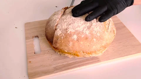 Baker in black gloves slicing a fresh loaf of homemade artisan sourdough bread. Stock Footage 334592429