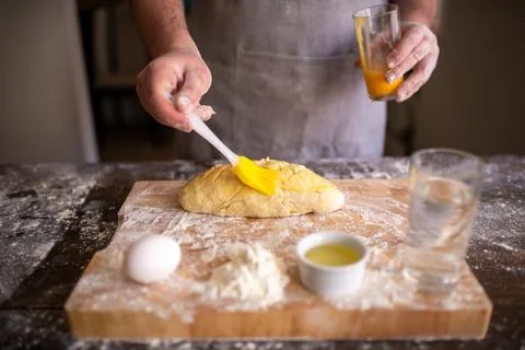 Baker brushing egg wash onto scored dough before baking Photos
