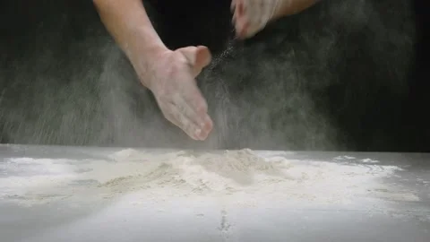 The baker claps his hands filled with white flour on a black background. Slow Stock Footage 149056037