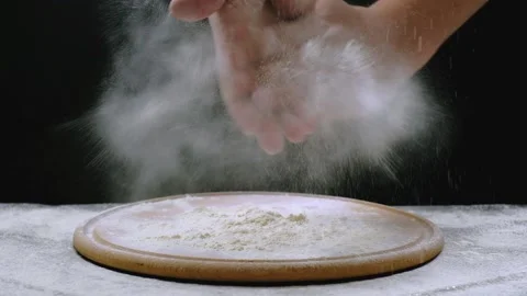 The baker claps his hands filled with white flour on a dark background. Slow Stock Footage 149056098