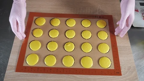Baker is cooking macaroons on stencil silicone mat on the table, preparing for Stock Footage 106001736