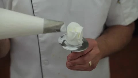 A baker creates a rose pedal with icing on a paddle Stock Footage 231414235
