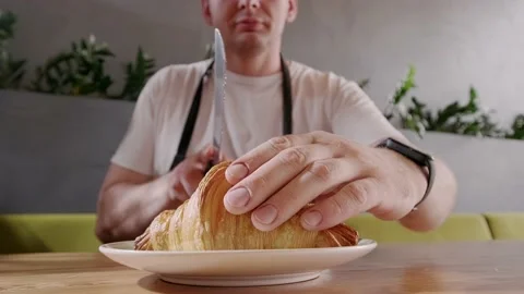 Baker cuts fresh crispy croissant and shows the filling the berry filling close Stock Footage 163276128