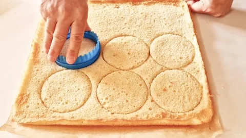 Baker cutting round sponge cake circles using a blue plastic cookie cutter tool Stock Footage 326633631