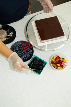 Baker decorates a chocolate cake with fresh berries and colorful toppings i.. Stock Photos