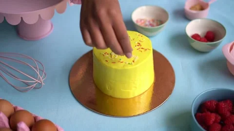 Baker decorating small yellow birthday cake with colorful sprinkles Stock-Footage 335956116