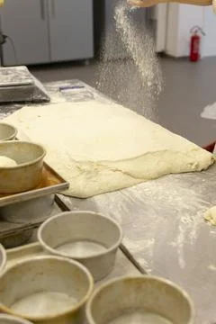 Baker dusting flour over stretched dough on prep table inside bakery kitchen Stock Photos