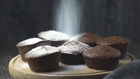 Baker dusting powdered icing sugar over delicious chocolate muffins Stock Footage 118585587