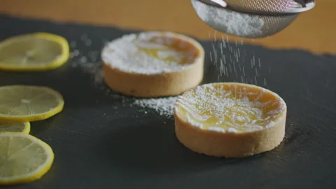 Baker dusts lemon tarts with powdered sugar on a black slate, garnished with Stock Footage 332017379
