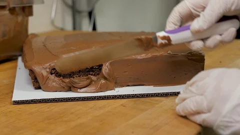 Baker fluffs up icing on the side of a chocolate cake Stock-Footage 94242110