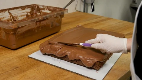 Baker frosts single layer chocolate cake as camera moves Stock Footage 94252650