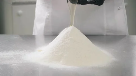 Baker in gloves adds egg to flour pile at table in kitchen Stock Footage 139486890