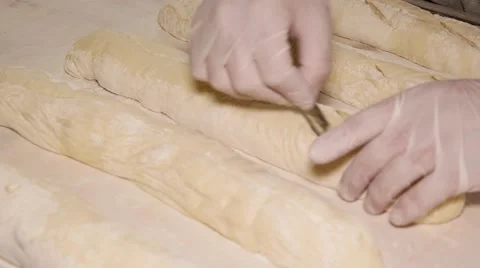 Baker in gloves making patterns on raw bread using a blade, closeup Stock Footage 64470768