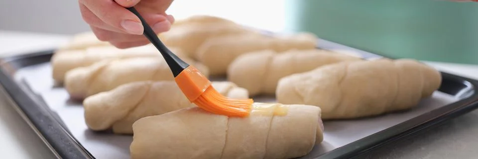 The baker greases the buns with an egg before baking Stock Photos