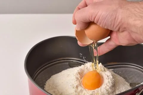 Baker hand  breaks an egg into a flour while making dough Foto stock