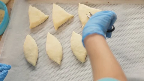 Baker hand cuts with scissors and inflicts egg mixture with brush on patties Stock Footage 90639537