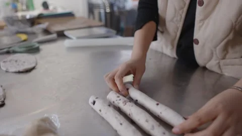 Baker hands skillfully rolling and preparing uncooked dough sticks with dried Stock Footage 328983914