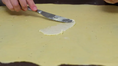 Baker hands spreading butter over rolled dough preparing croissant or cinnabon Stock Footage 326003835