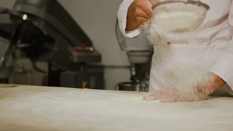 Baker hands in the uniform sifting measured flour on a table. Cooking Stock Footage
