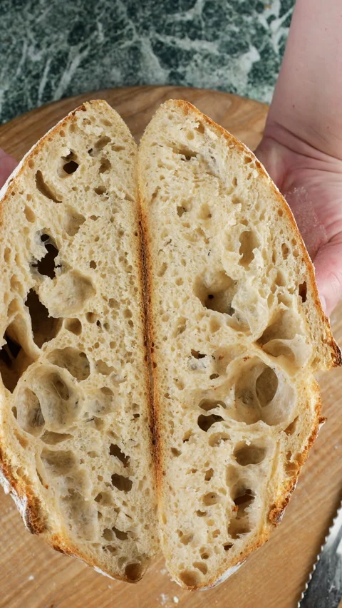 A baker holds two halves of freshly baked homemade wheat sourdough bread. Stock Footage 341500851