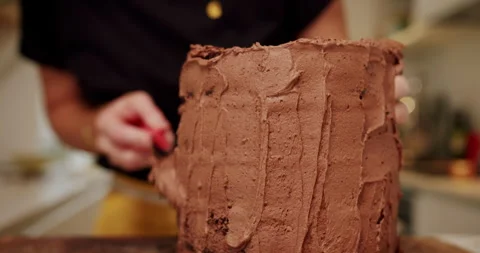 Baker icing a chocolate cake with chocolate frosting in yellow apron Stock Footage 247785981