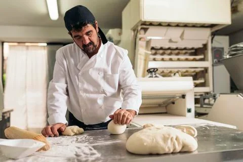 Baker kneading dough in a bakery. Stock Photos