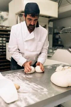 Baker kneading dough in a bakery. Stock Photos