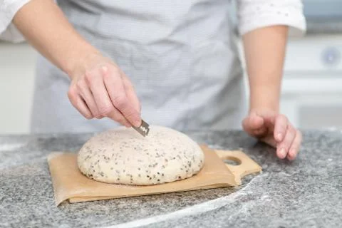 Baker making patterns on raw bread using a knife ot blade to shape the dough  Stock Photos