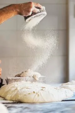 Baker man hand spreading flour to dough. Stock Photos