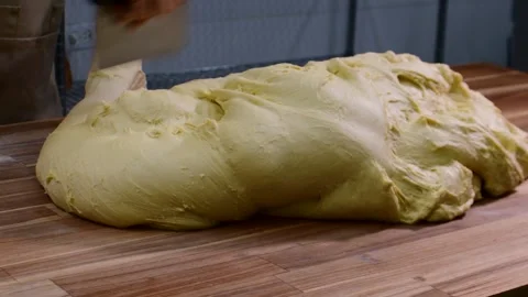 Baker Man hands cutting dough on a wooden table to prepare bread, showing Stock Footage 328528280