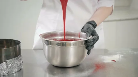 Baker mixes red dough with spatula at table in kitchen Stock Footage 138727870