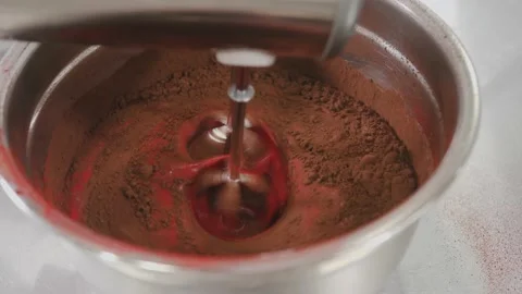Baker mixes red liquid dough with cocoa powder in metal bowl Stock Footage 139487140