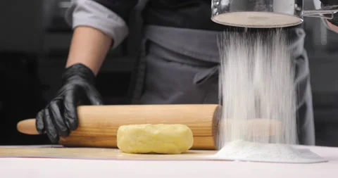 The baker or chef is about to roll the dough on a white table, dusting it with Video stock 165873064