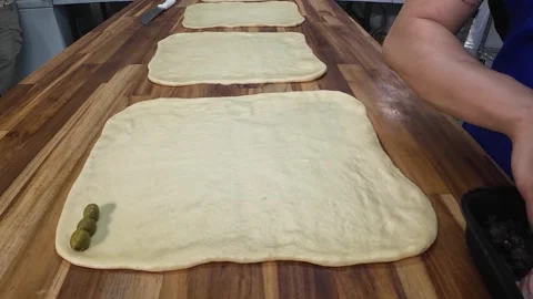 Baker placing green olives on raw dough for ham bread Stock Footage 339784153