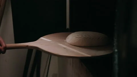 Baker placing a loaf of bread dough into a hearth Stock Footage 130395110