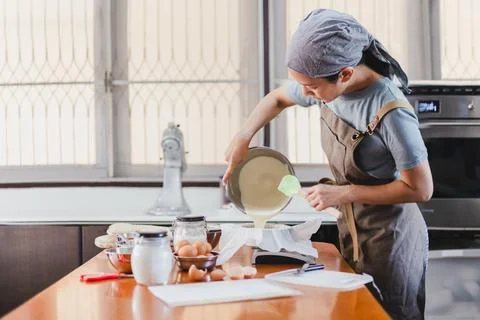 Baker pouring cake mixture into a cake tin with paper for baking cheesecake. Stock Photos