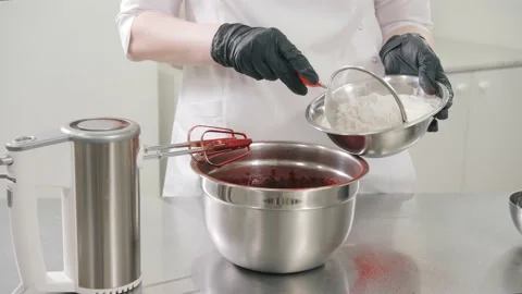 Baker pours wheat through sieve to red dough in metal bowl Stock Footage 137932230